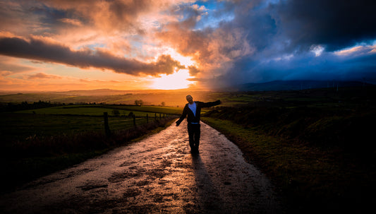 A man standing on a mountain road in at sunset. The sky is bursting with colour.